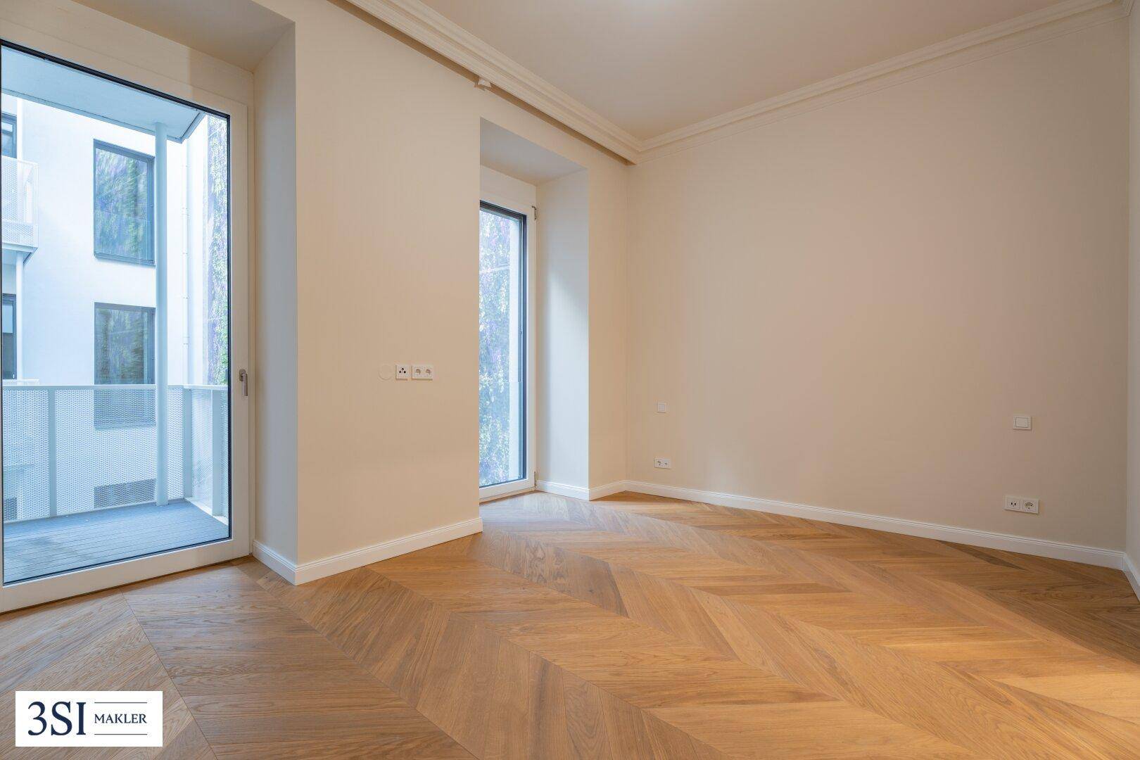 Leerer Raum mit Fischgrätparkett und Zugang zu einem Balkon, der viel Licht spendet.