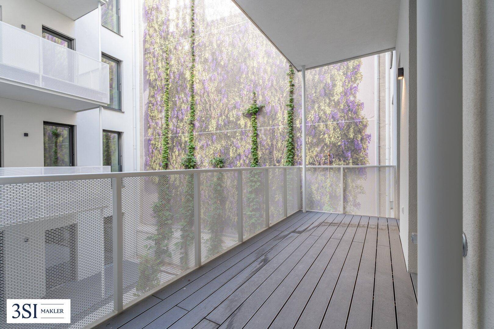 Moderner Balkon mit Holzboden und grüner Wandbegrünung im Innenhof.