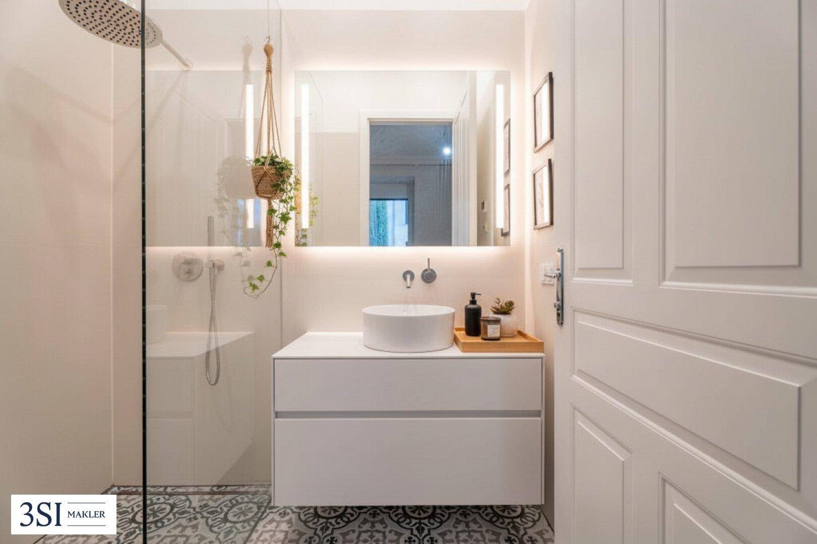 Modernes Badezimmer mit runder Aufsatzwaschschale, beleuchtetem Spiegel und Regendusche.