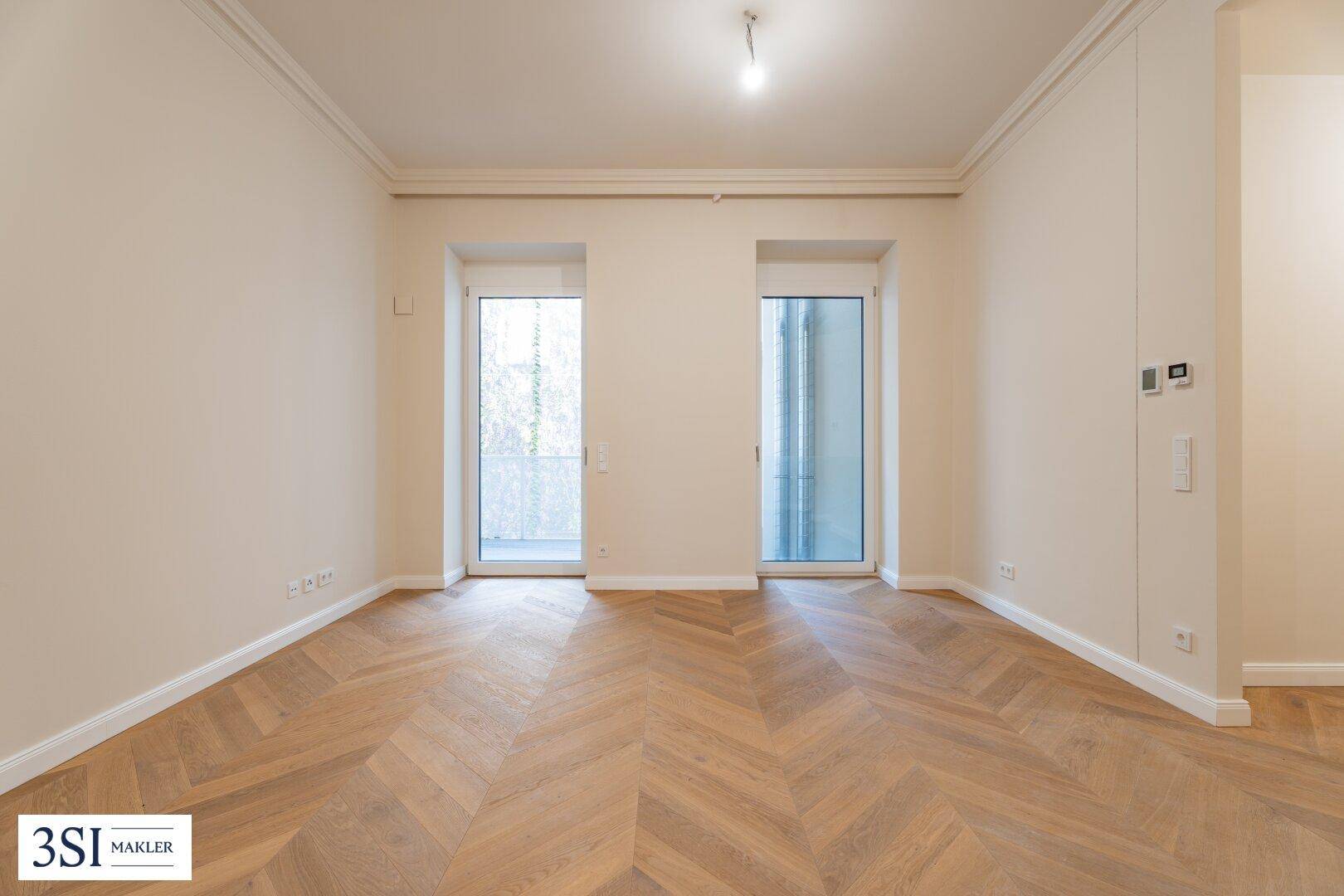 Helles Zimmer mit Fischgrätparkett und zwei französischen Balkonen, ideal für Wohn- oder Schlafbereich.