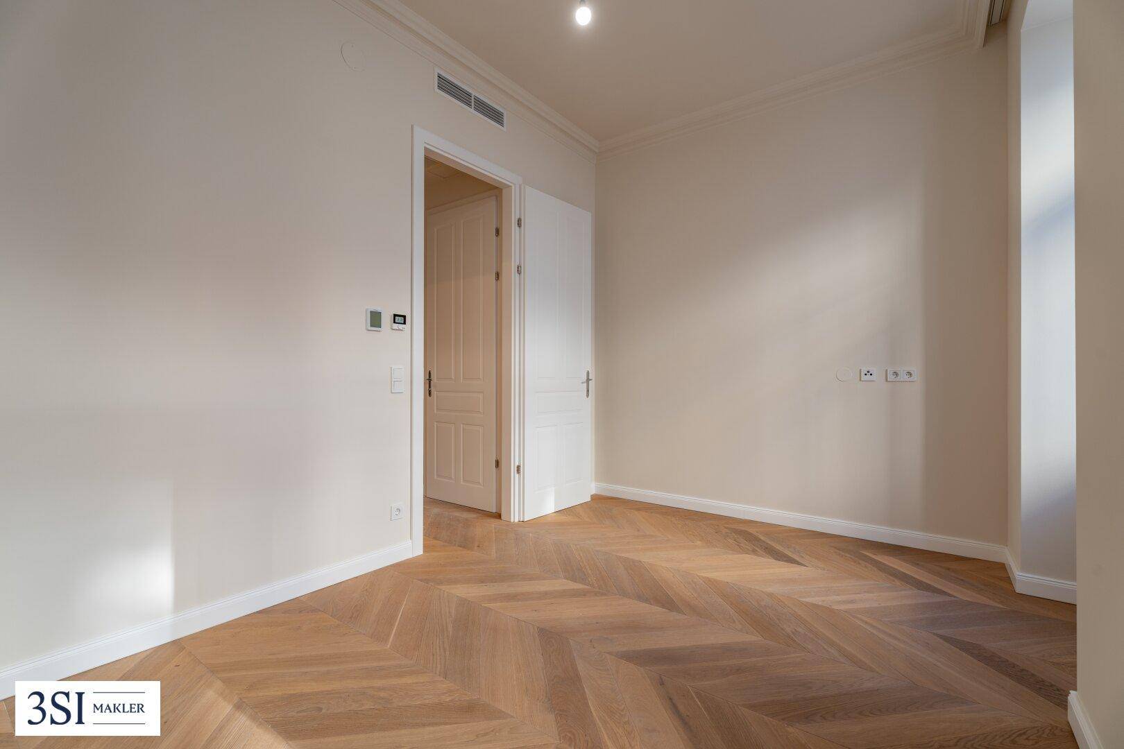 Freundliches Zimmer mit Fischgrätparkett und offener Tür, bereit für individuelle Gestaltung.