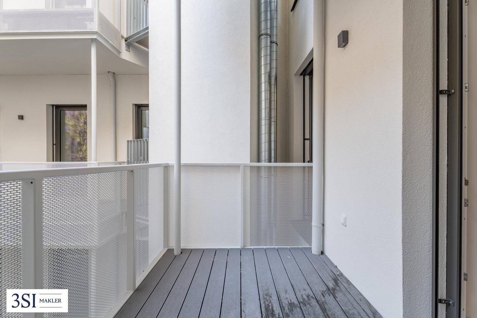 Moderner Balkon mit grauen Dielen und weißem Geländer, bietet einen Blick in den Innenhof.