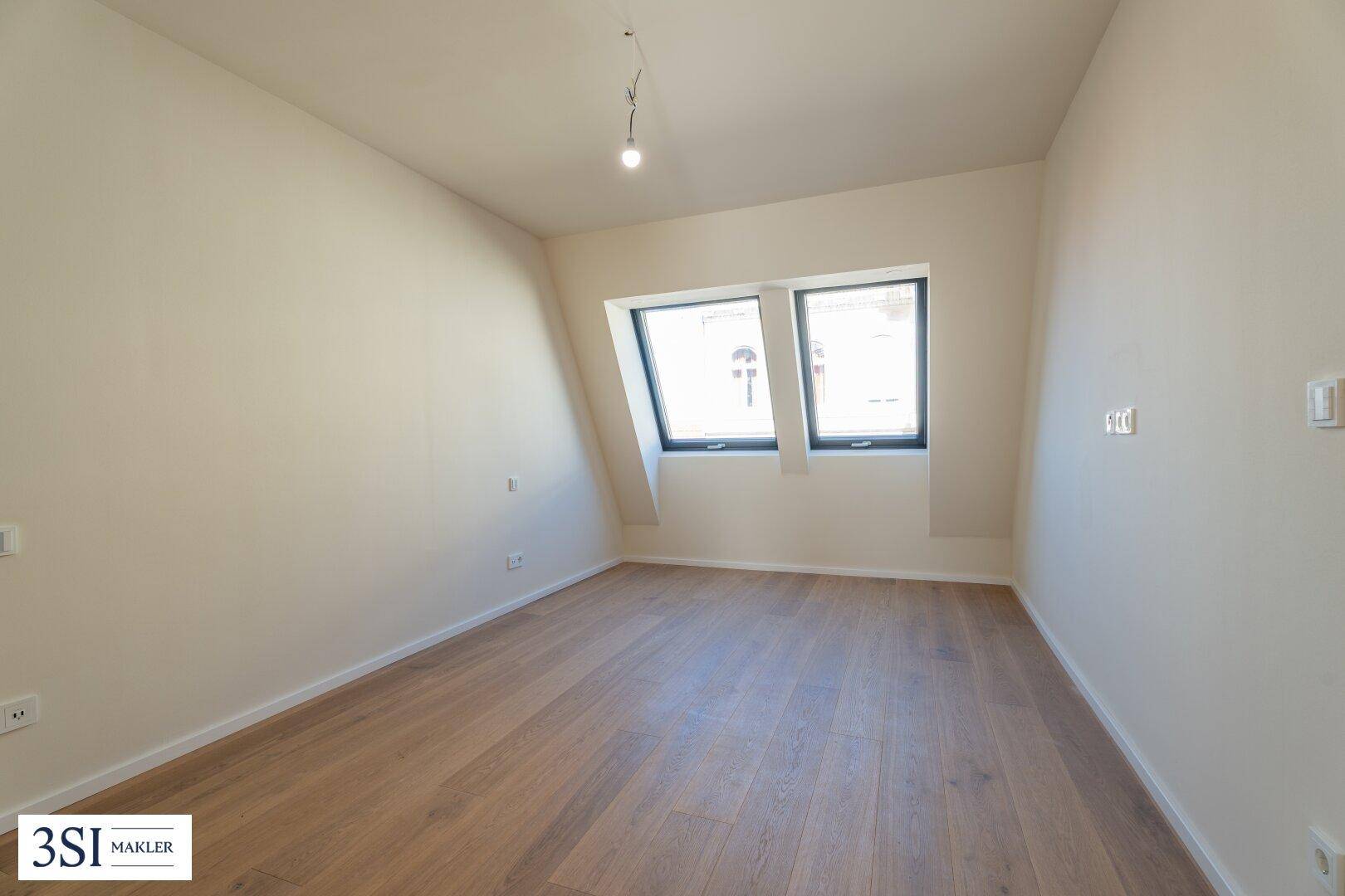 Helles Zimmer im Dachgeschoss mit Holzboden und zwei schrägen Dachfenstern, die viel Licht spenden.