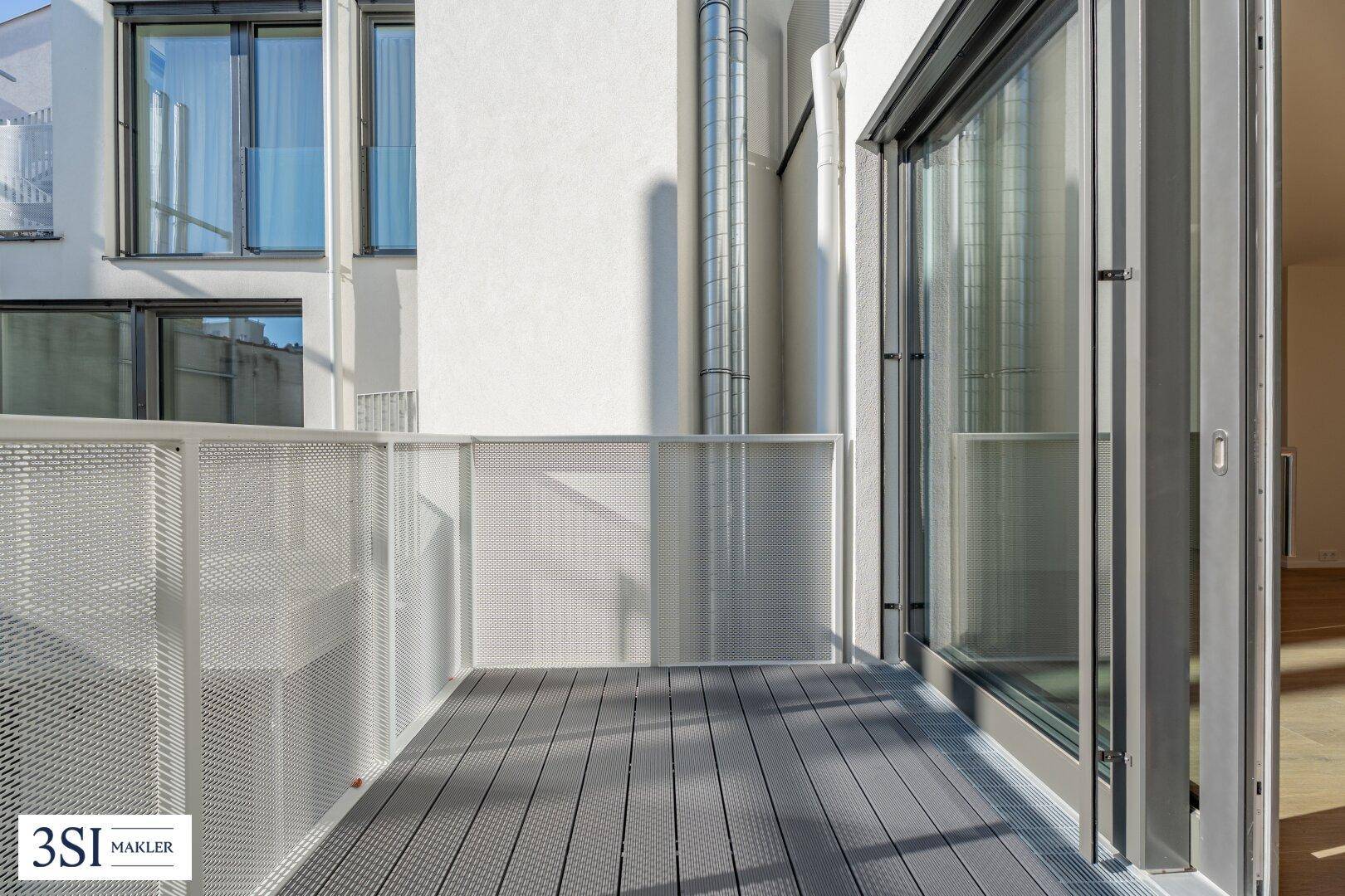 Moderner Balkon mit grauem Holzboden und Metallgeländer, bietet einen Blick auf die Umgebung.