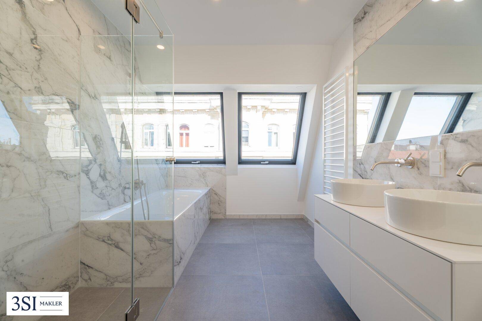Luxuriöses Badezimmer mit Marmorfliesen, Doppelwaschbecken und Badewanne unter schrägen Dachfenstern.