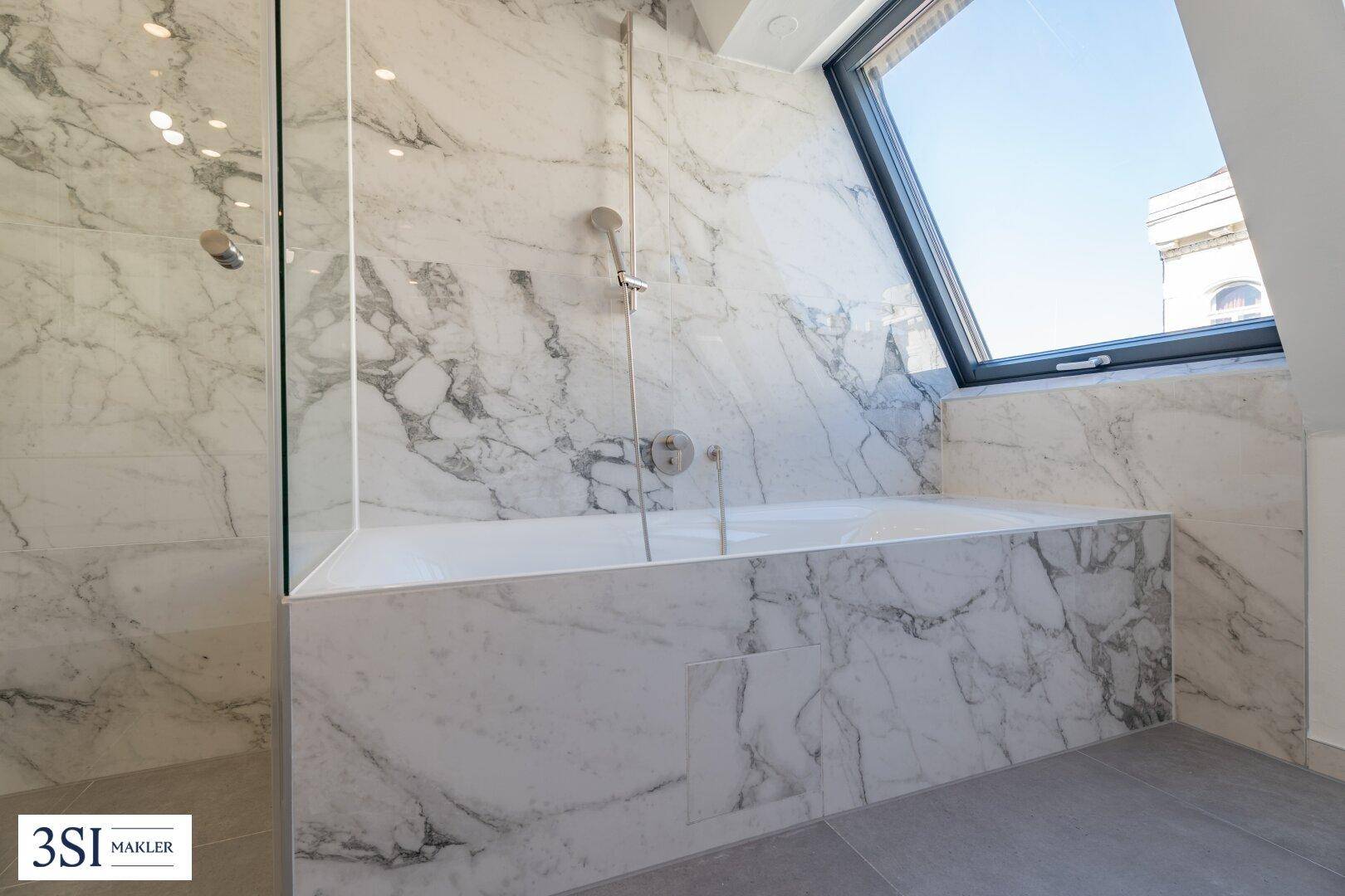 Elegante Badewanne mit Marmorverkleidung und integrierter Dusche unter einem großen Dachfenster.