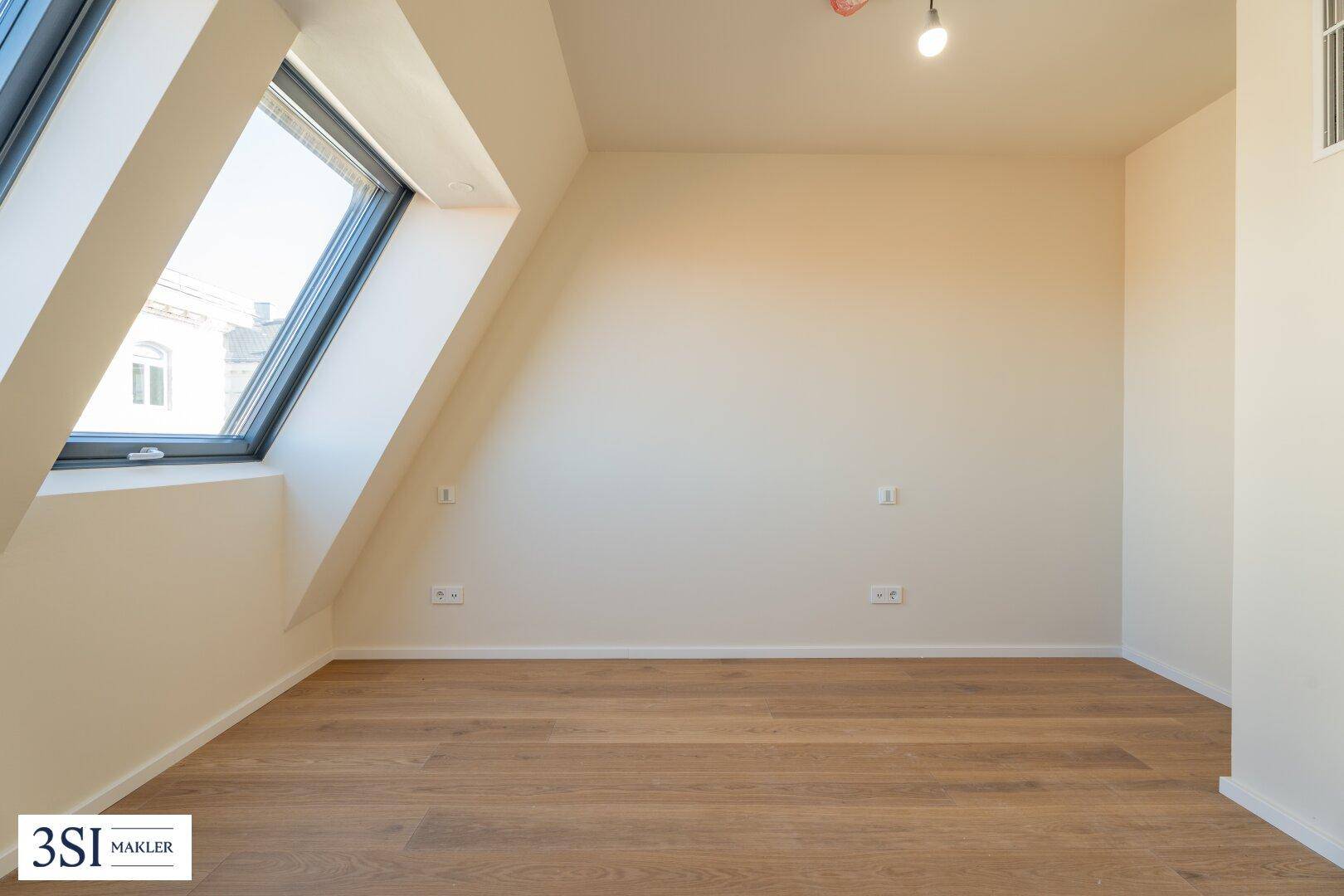 Helles Zimmer im Dachgeschoss mit Holzboden, schräger Decke und einem großen Dachfenster.