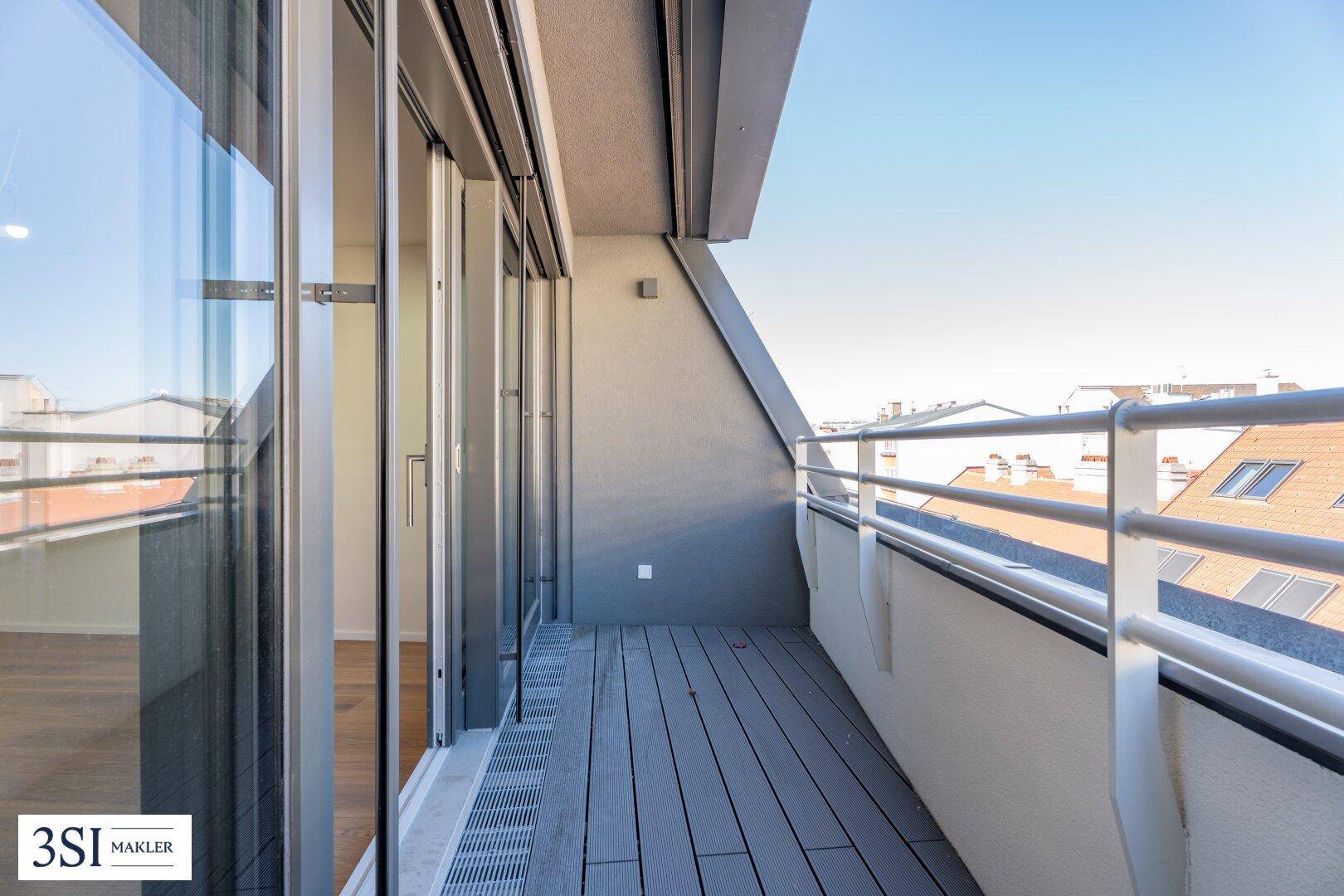 Langer, schmaler Balkon mit Holzdielen und Metallgeländer, bietet einen Blick über die Dächer.