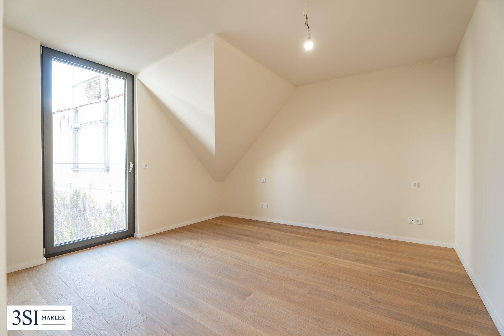 Lichtdurchflutetes Dachgeschosszimmer mit Holzboden und schräger Decke, bietet einen Blick nach draußen.