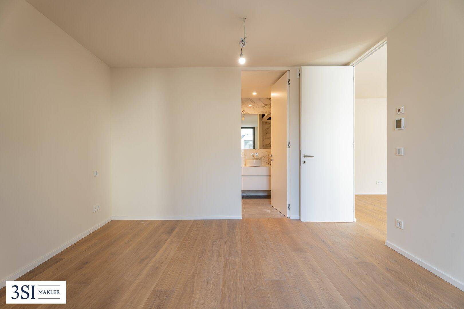 Helles Schlafzimmer mit Holzboden und direktem Zugang zu einem modernen Badezimmer.