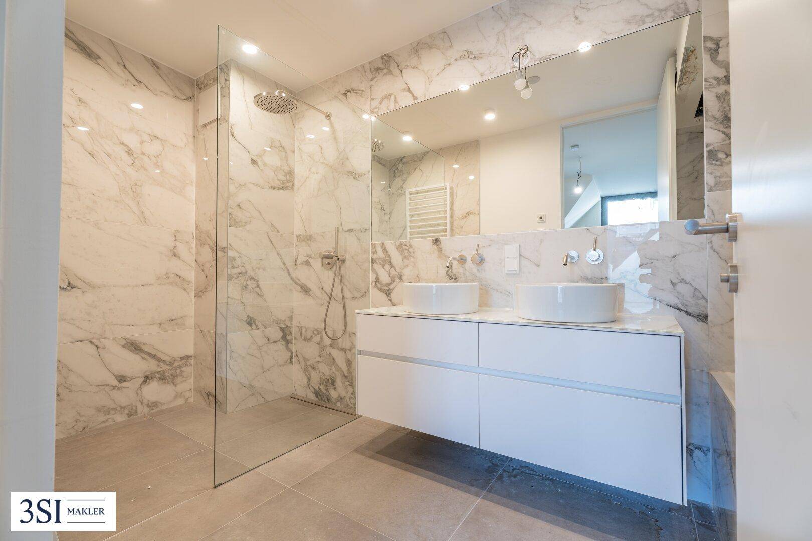 Luxuriöses Badezimmer mit Marmorfliesen, Doppelwaschbecken und großer begehbarer Dusche.