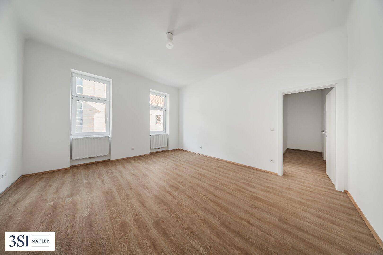 Geräumiger, heller Raum mit Holzboden und großen Fenstern, bereit zur individuellen Gestaltung.