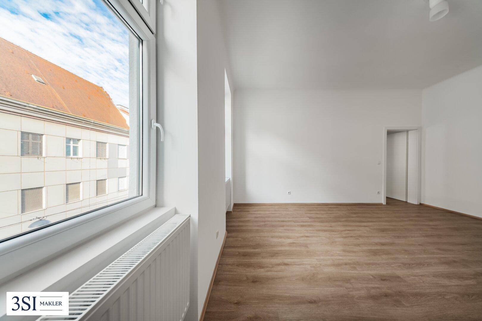Heller Raum mit großem Fenster, das viel Tageslicht hereinlässt und einen Blick nach draußen bietet.