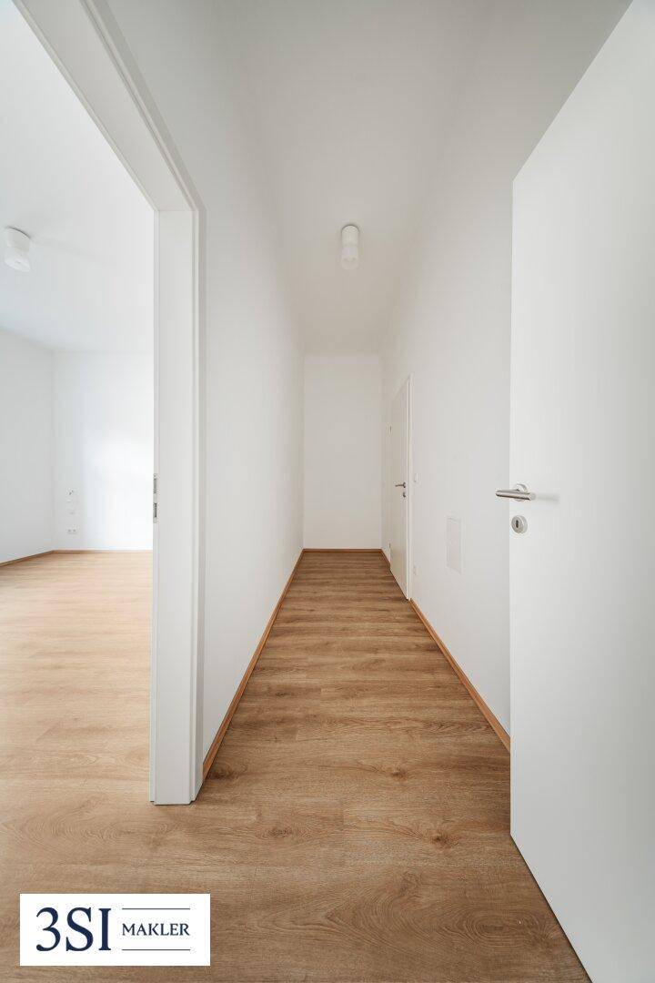 Langer, heller Flur mit Holzboden, der zu weiteren Räumen der Wohnung führt.