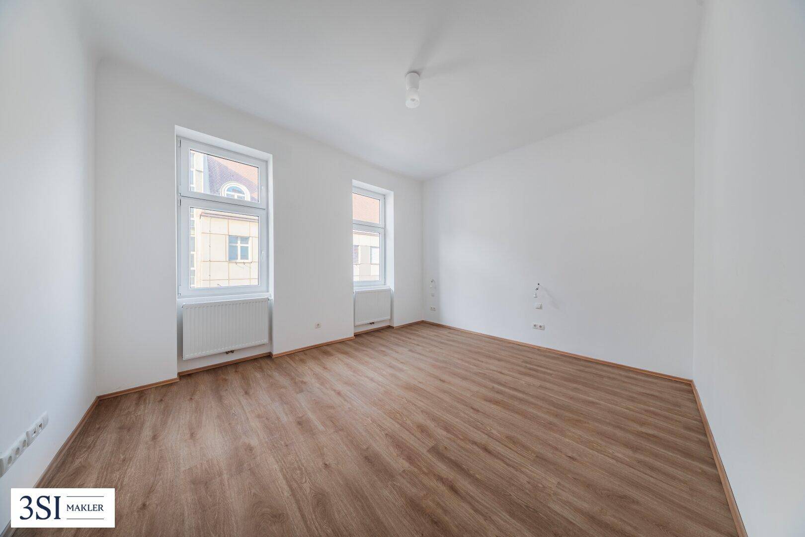 Leerer, heller Raum mit Holzboden und zwei Fenstern, ideal für Wohn- oder Schlafbereich.