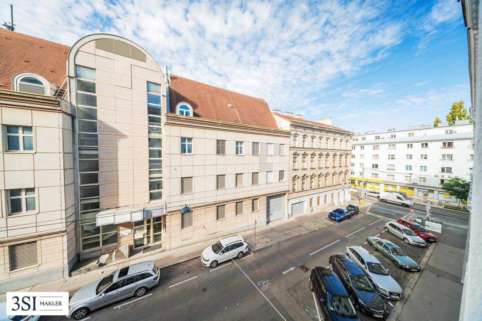 Blick von oben auf eine belebte Stadtstraße mit parkenden Autos und umliegenden Gebäuden.