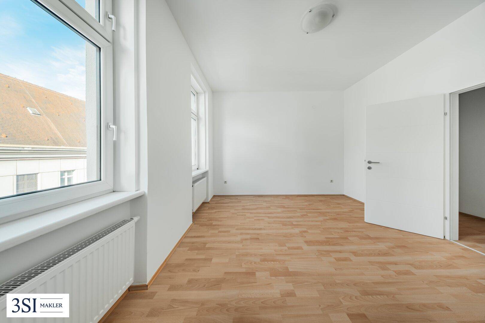 Heller Raum mit Parkettboden und großem Fenster, das einen weiten Blick auf die Umgebung ermöglicht.