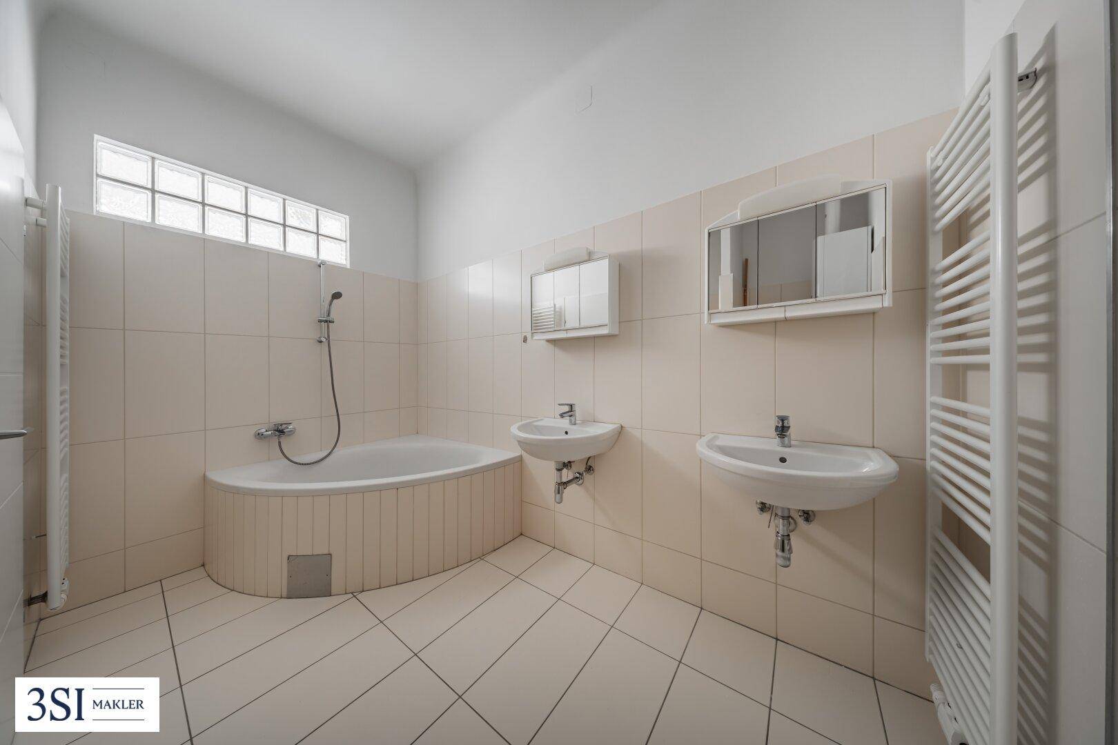 Helles Badezimmer mit zwei Waschbecken, Badewanne und beheiztem Handtuchhalter.