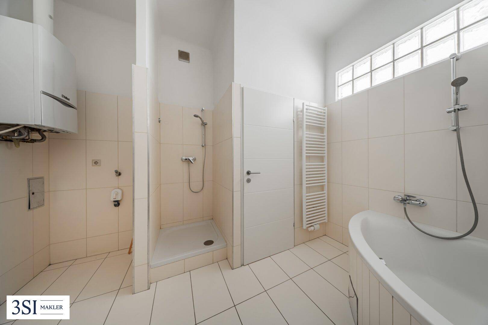 Geräumiges Badezimmer mit Dusche, Badewanne und beheiztem Handtuchhalter in hellen Fliesen.