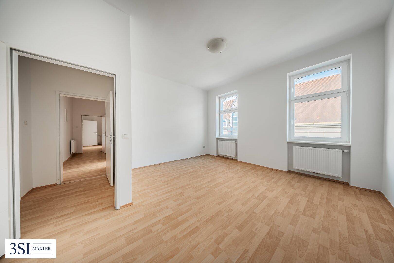 Geräumiges Zimmer mit Parkettboden und zwei Fenstern, das einen Zugang zum Flur bietet.