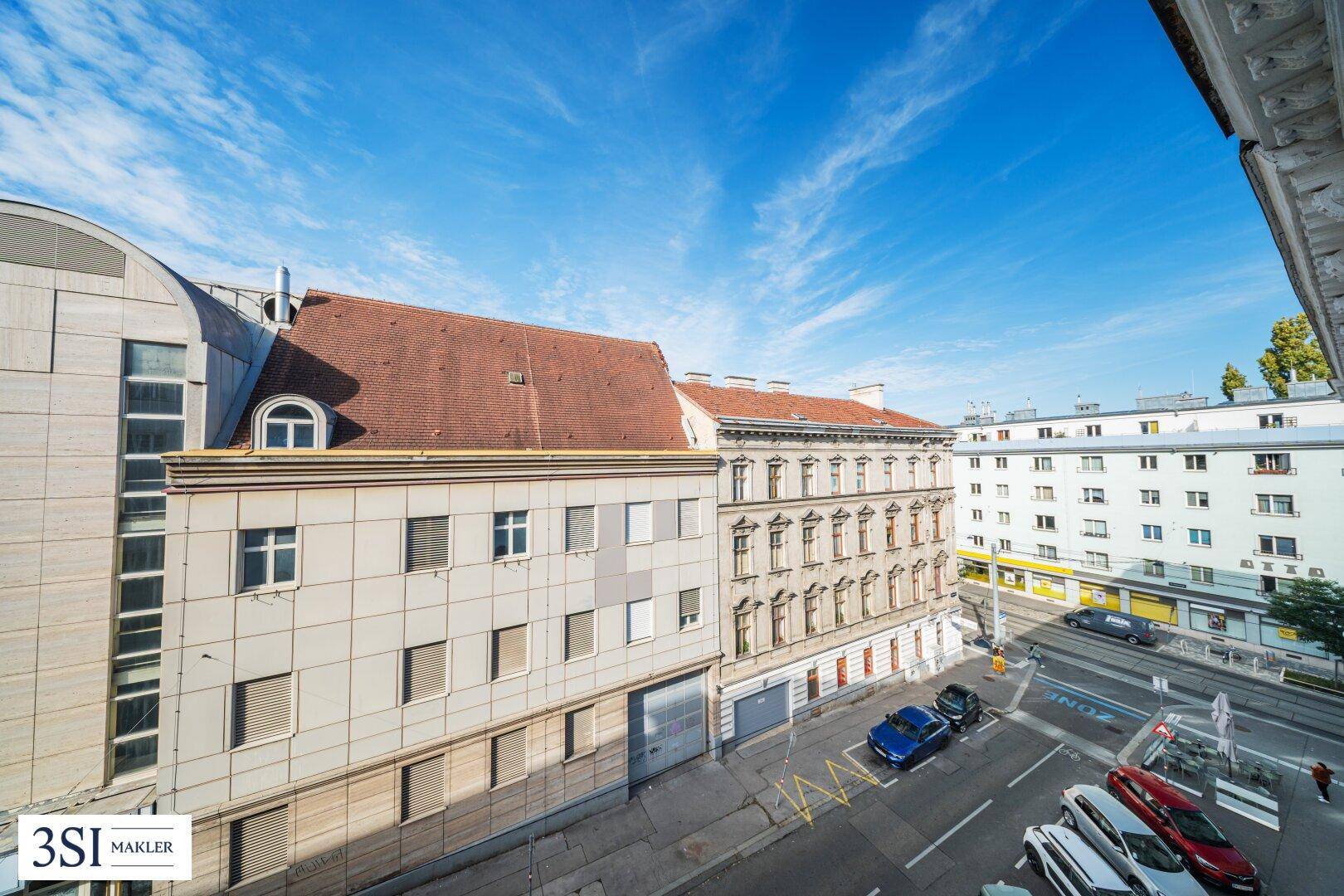 Weitblick über eine belebte Straße mit historischen und modernen Gebäuden unter blauem Himmel.