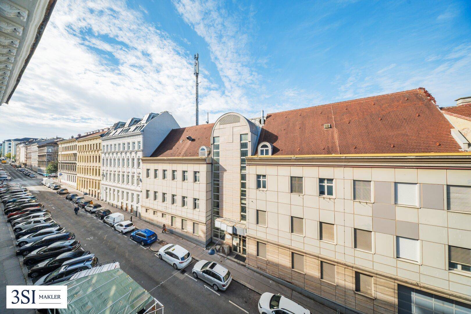 Panoramablick über eine städtische Straße mit parkenden Autos und einer Mischung aus Alt- und Neubauten.