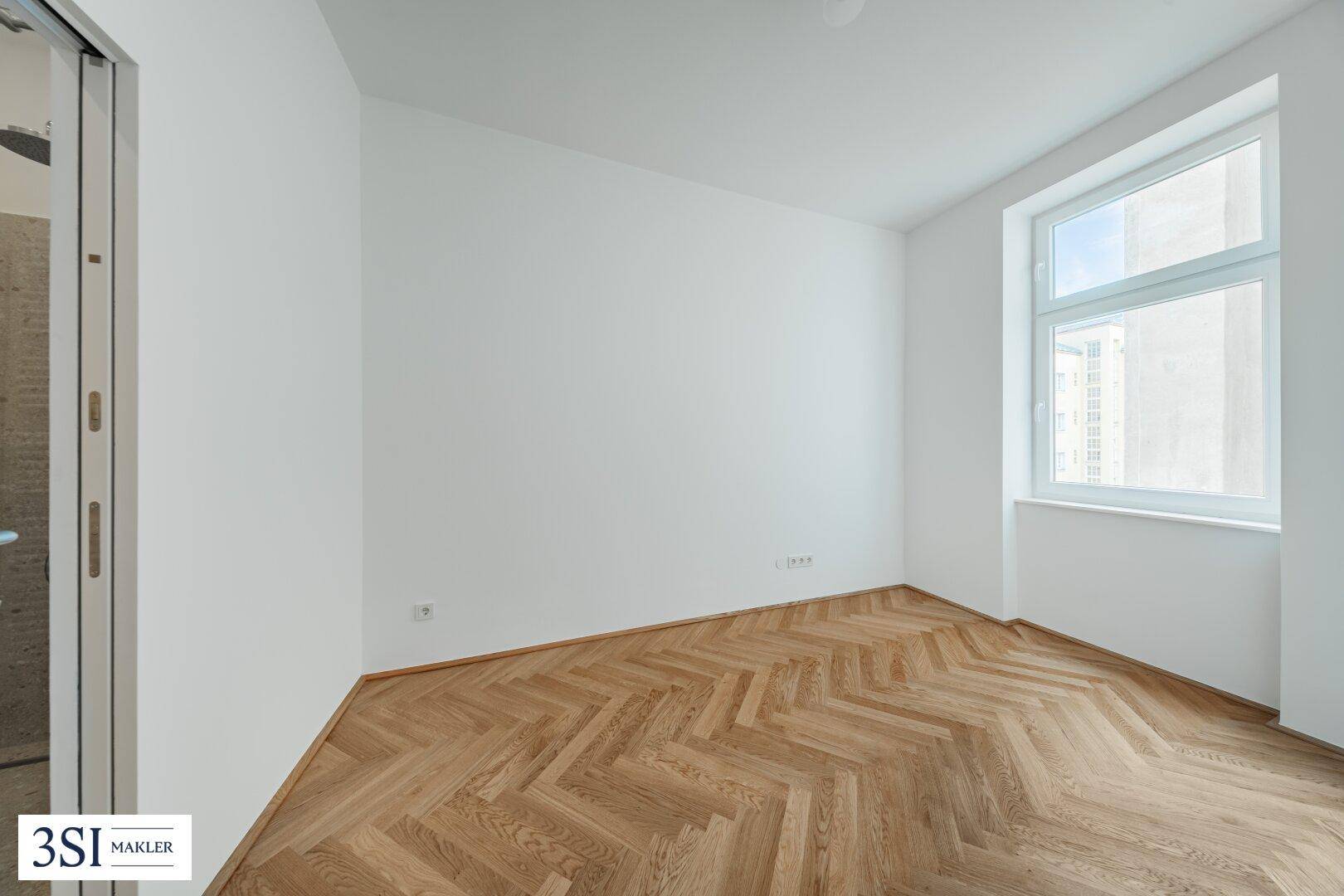 Helles Schlafzimmer mit Fischgrätparkett und einem großen Fenster, bereit zur Einrichtung.