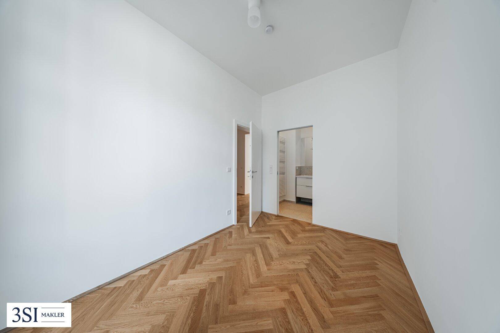 Schlafzimmer mit Fischgrätparkett und direktem Zugang zu einem modernen Badezimmer.
