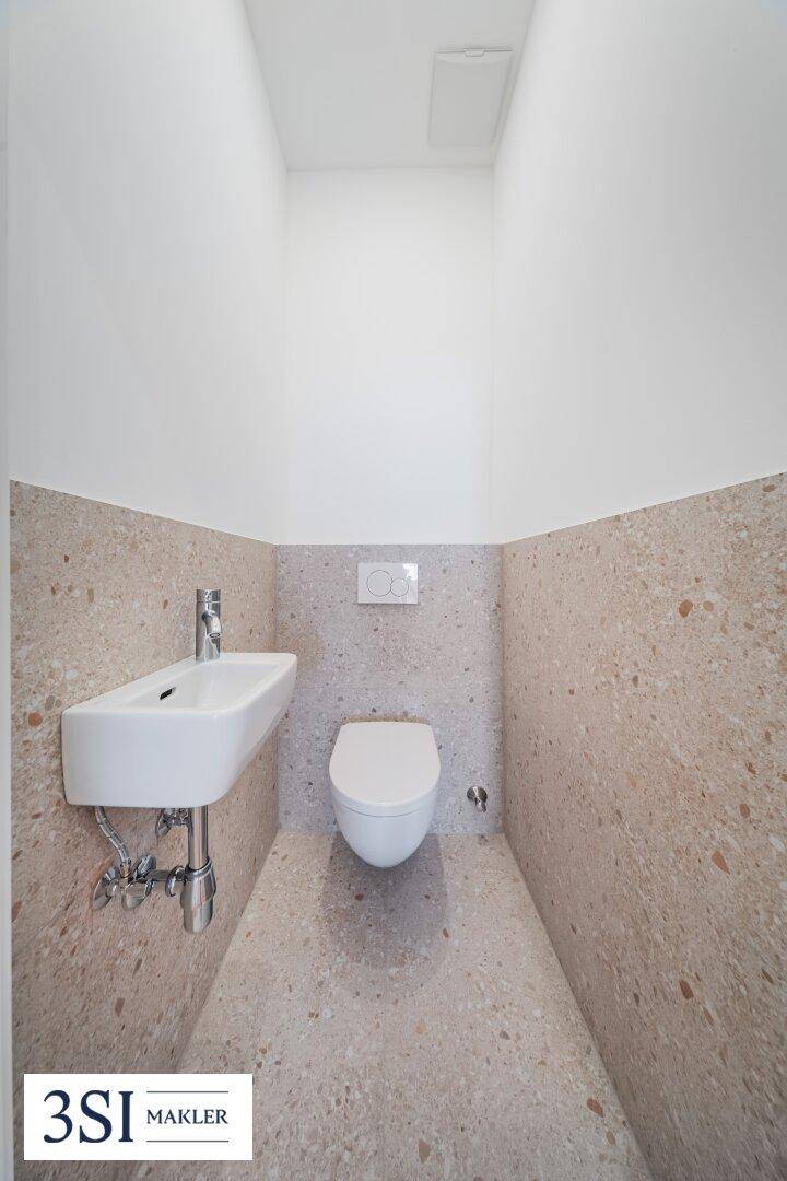 Modernes Gäste-WC mit wandhängender Toilette und kleinem Waschbecken, in hellen Fliesen gehalten.