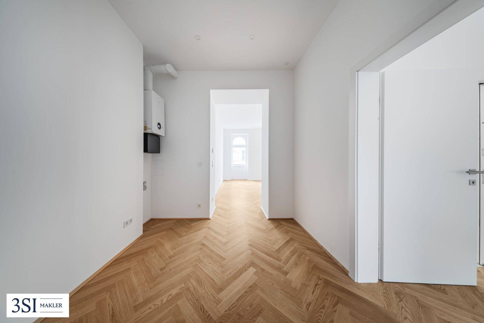 Heller Flur mit Fischgrätparkett und einem Heizkessel an der Wand, führt zu weiteren Räumen.