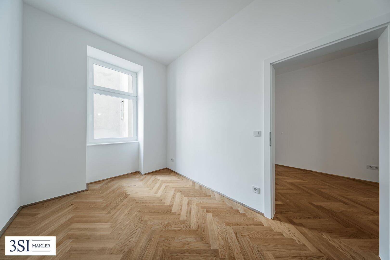 Heller Raum mit Fischgrätparkett und einem Fenster, das viel Tageslicht hereinlässt.