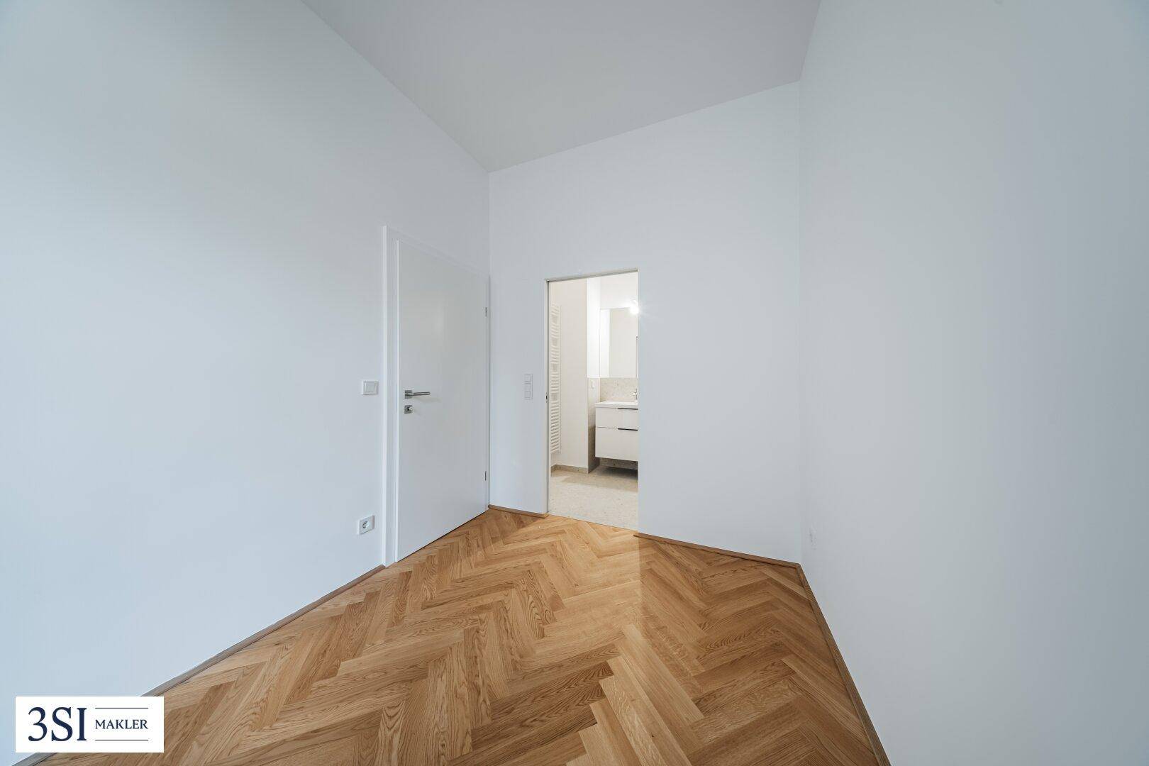 Unmöblierter Raum mit Fischgrätparkett und Zugang zu einem modernen Badezimmer.