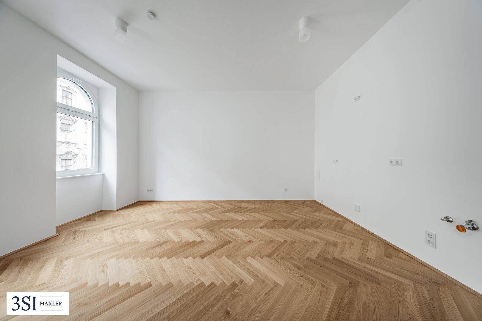 Lichtdurchfluteter Raum mit neuem Fischgrätparkett und einer großen Rundbogenfensterfront.