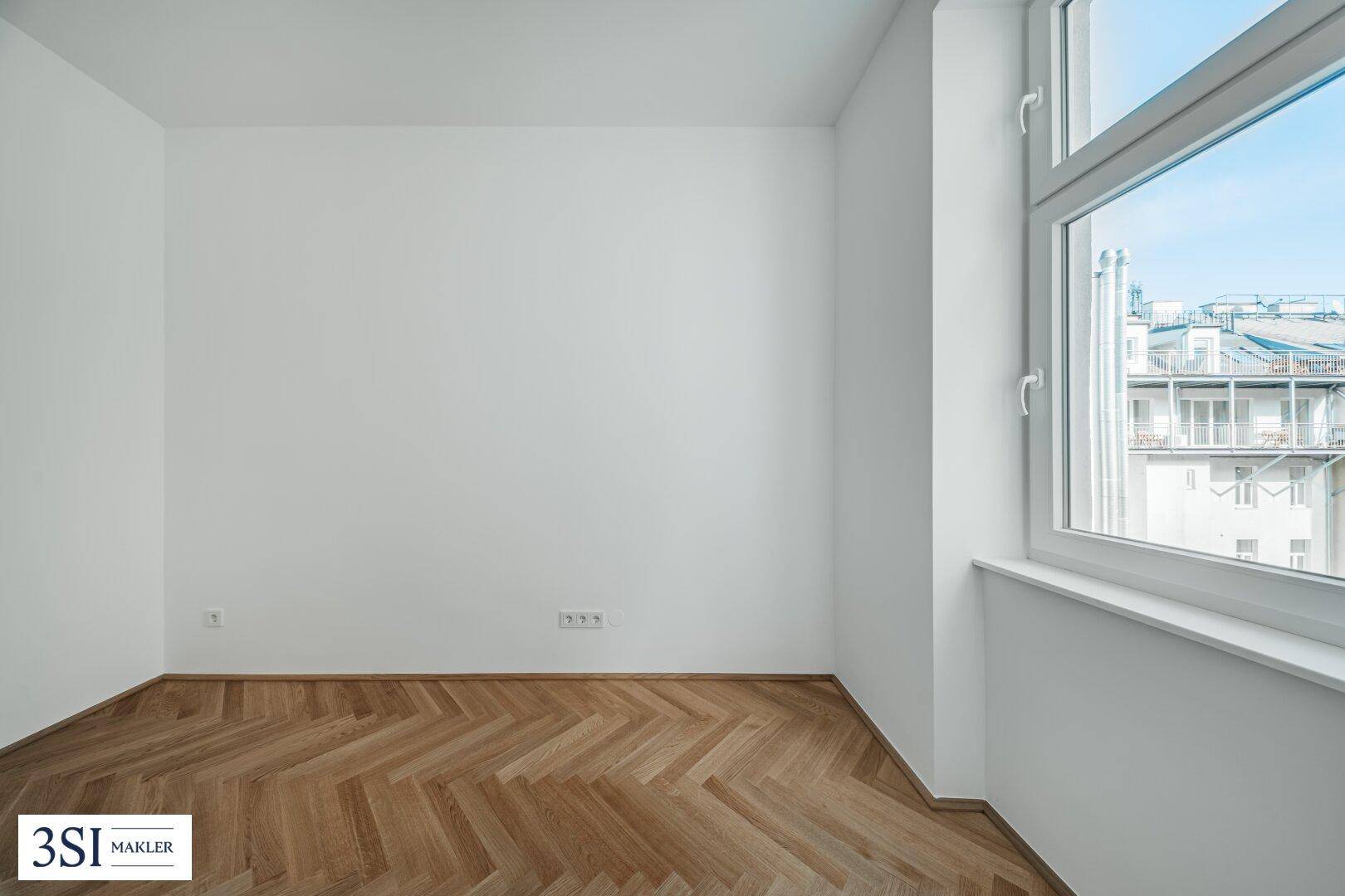 Eckbereich eines hellen Zimmers mit Fischgrätparkett und einem Fenster mit Stadtblick.