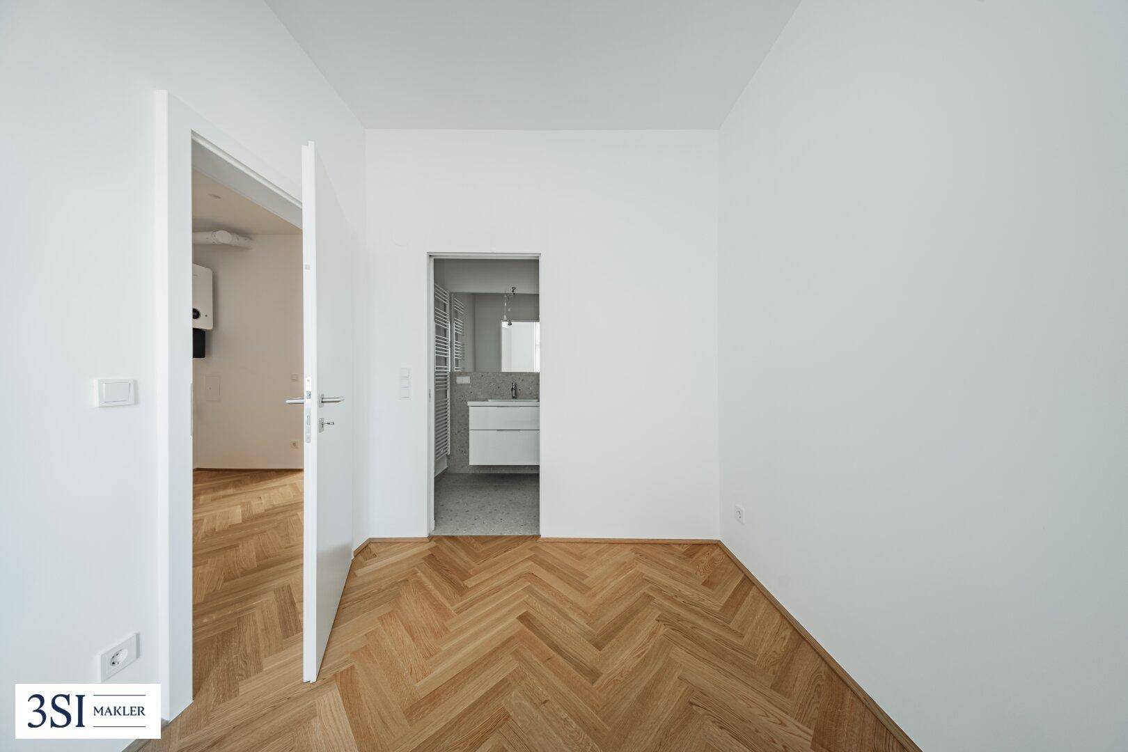 Zimmer mit Fischgrätparkett und Zugang zu einem modernen Badezimmer, ideal als Schlaf- oder Ankleidezimmer.