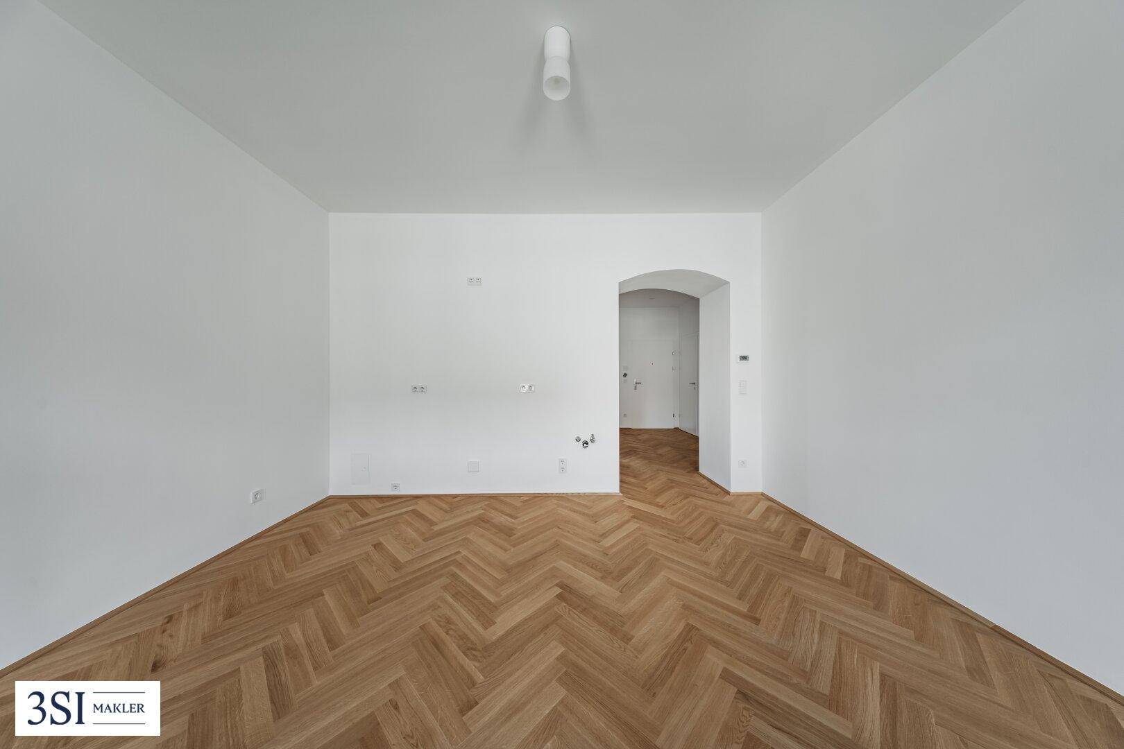 Heller Raum mit Fischgrätparkett und einem Bogendurchgang, der eine offene Gestaltung andeutet.