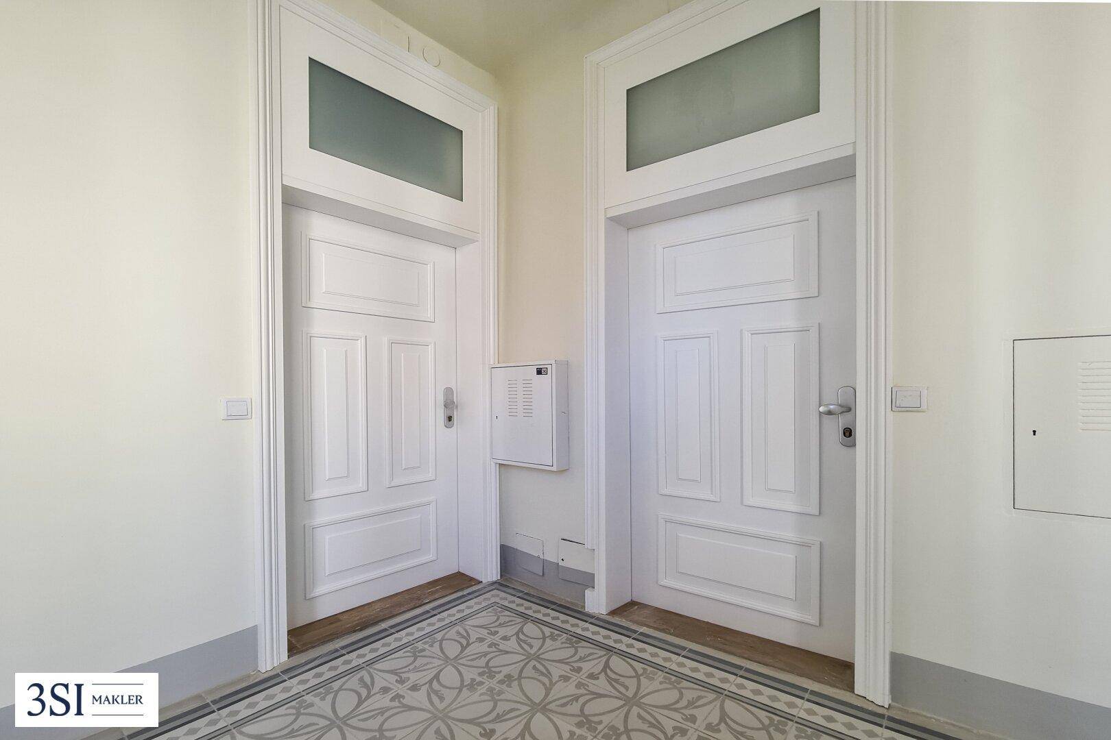 Eingangsbereich mit zwei eleganten, weißen Türen und gemusterten Fliesen, klassischer Altbau-Stil.