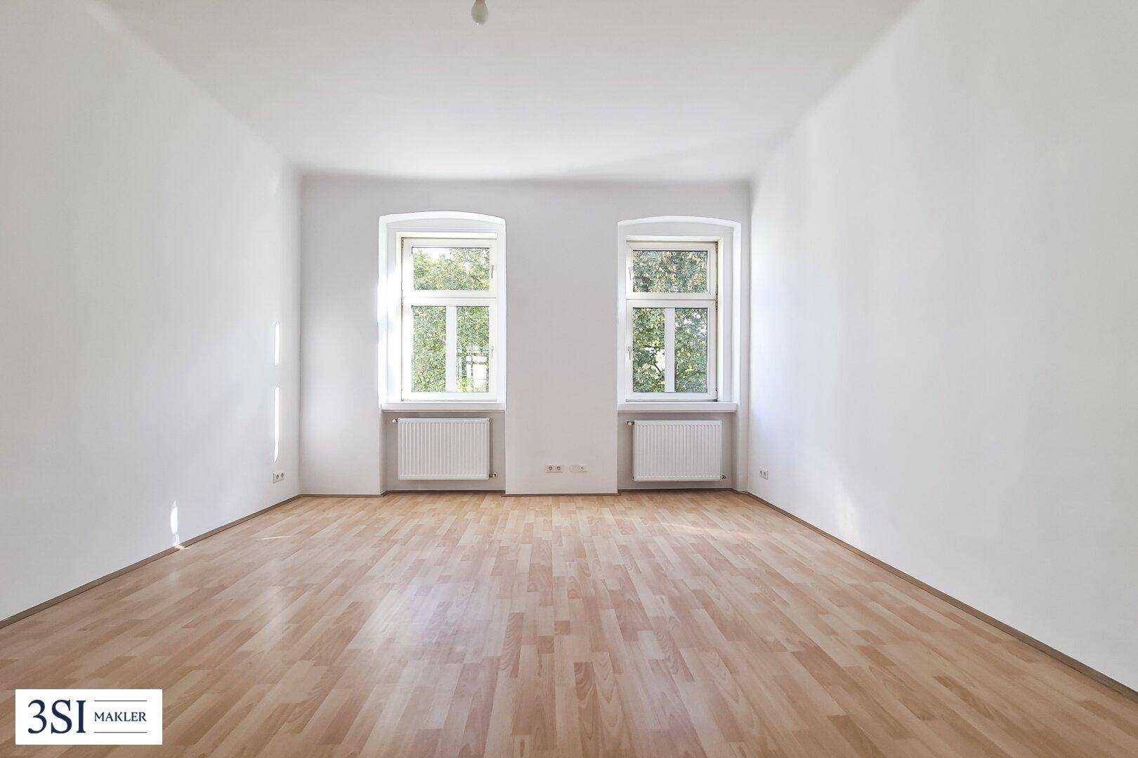 Leeres Zimmer mit hellem Parkettboden und zwei Fenstern, bereit zur Einrichtung.