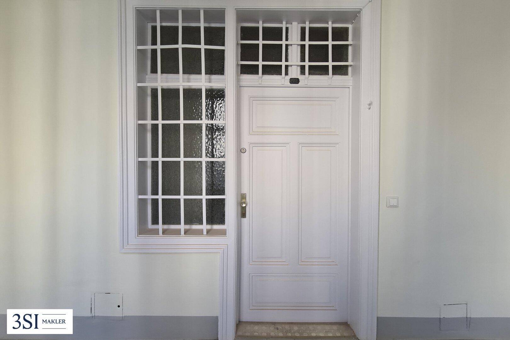 Klassische Eingangstür mit dekorativen Fenstergittern und weißem Anstrich.
