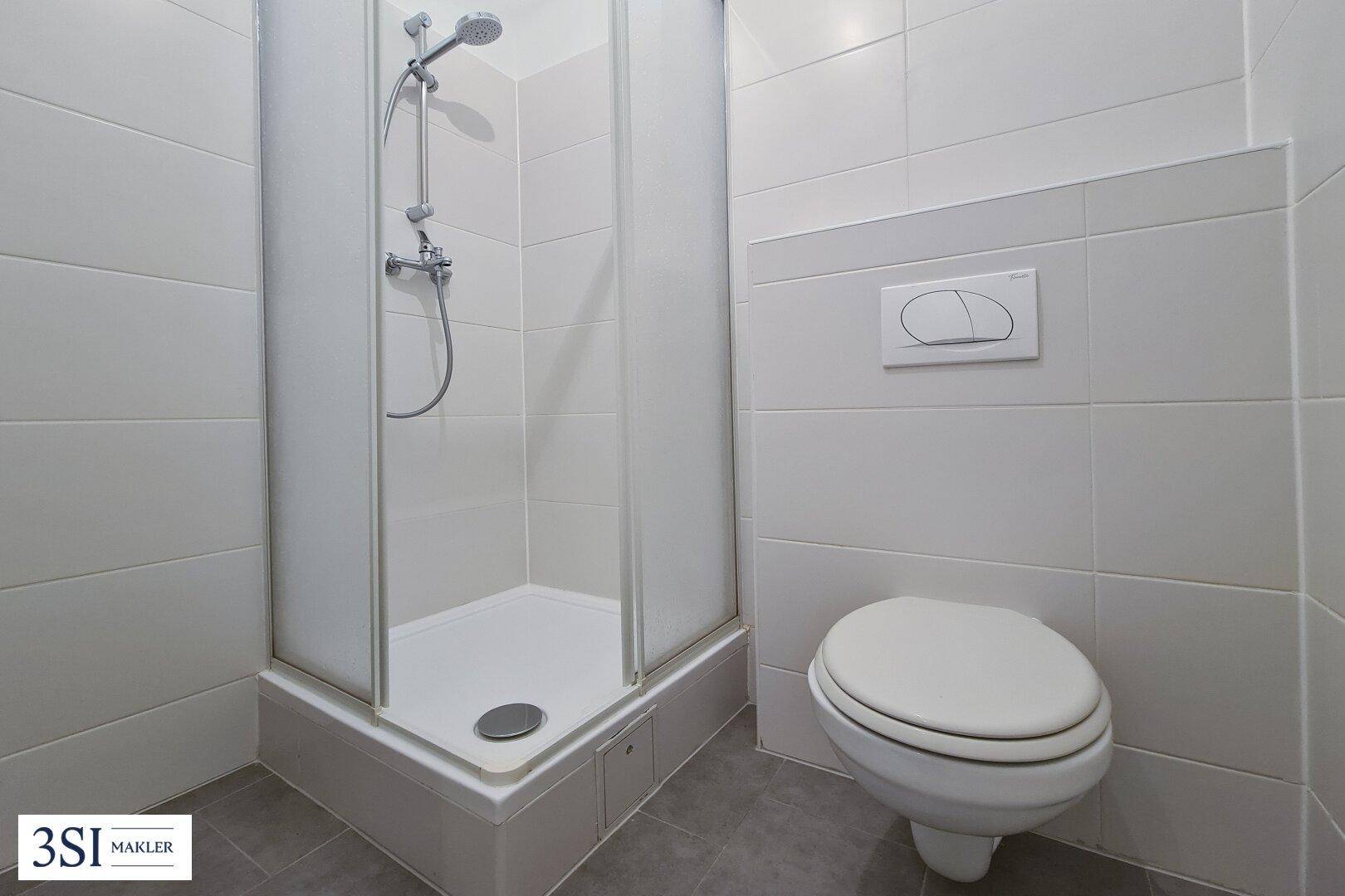 Badezimmer mit Duschkabine und wandhängendem WC, ausgestattet mit weißen Fliesen.