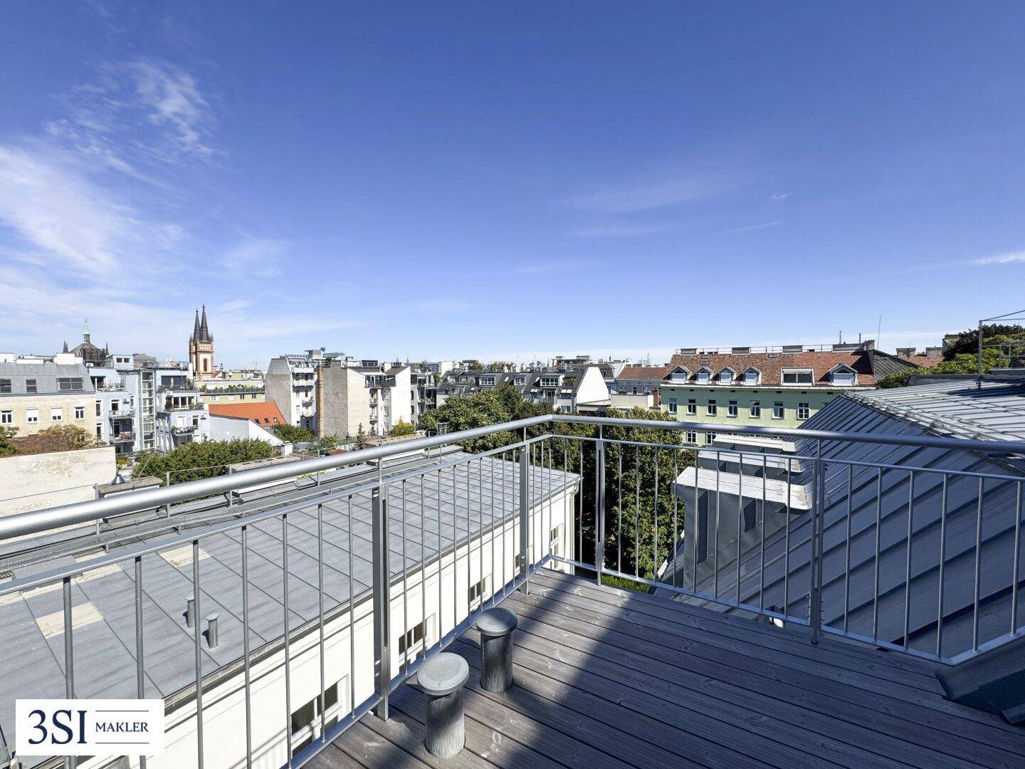 Weitläufige Dachterrasse mit Holzboden und Panoramablick über die Dächer der Stadt.