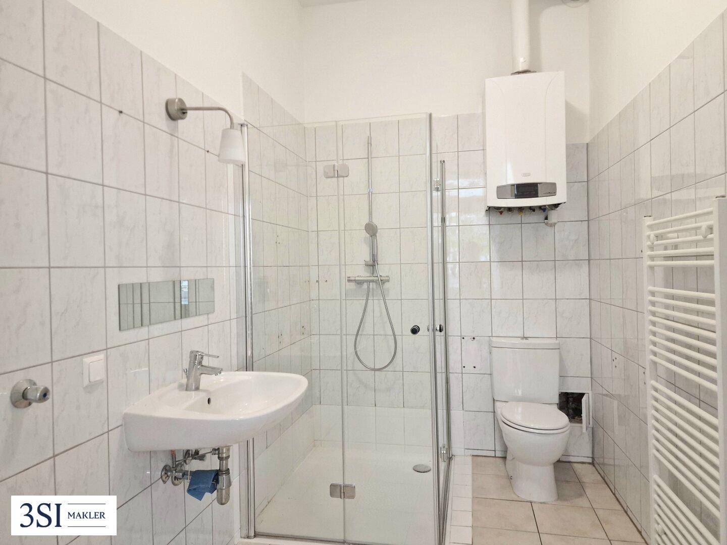 Funktionales Badezimmer mit Duschkabine, WC, Waschbecken und Handtuchheizkörper.