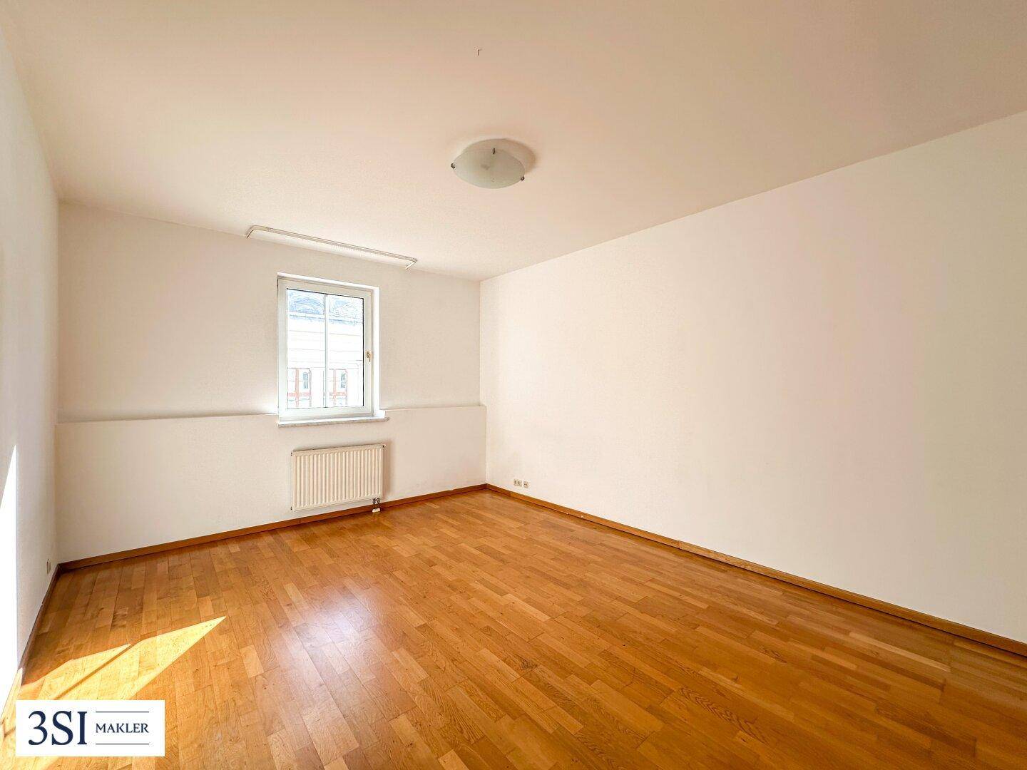 Leerer Raum mit Holzboden und einem Fenster, das Tageslicht hereinlässt.