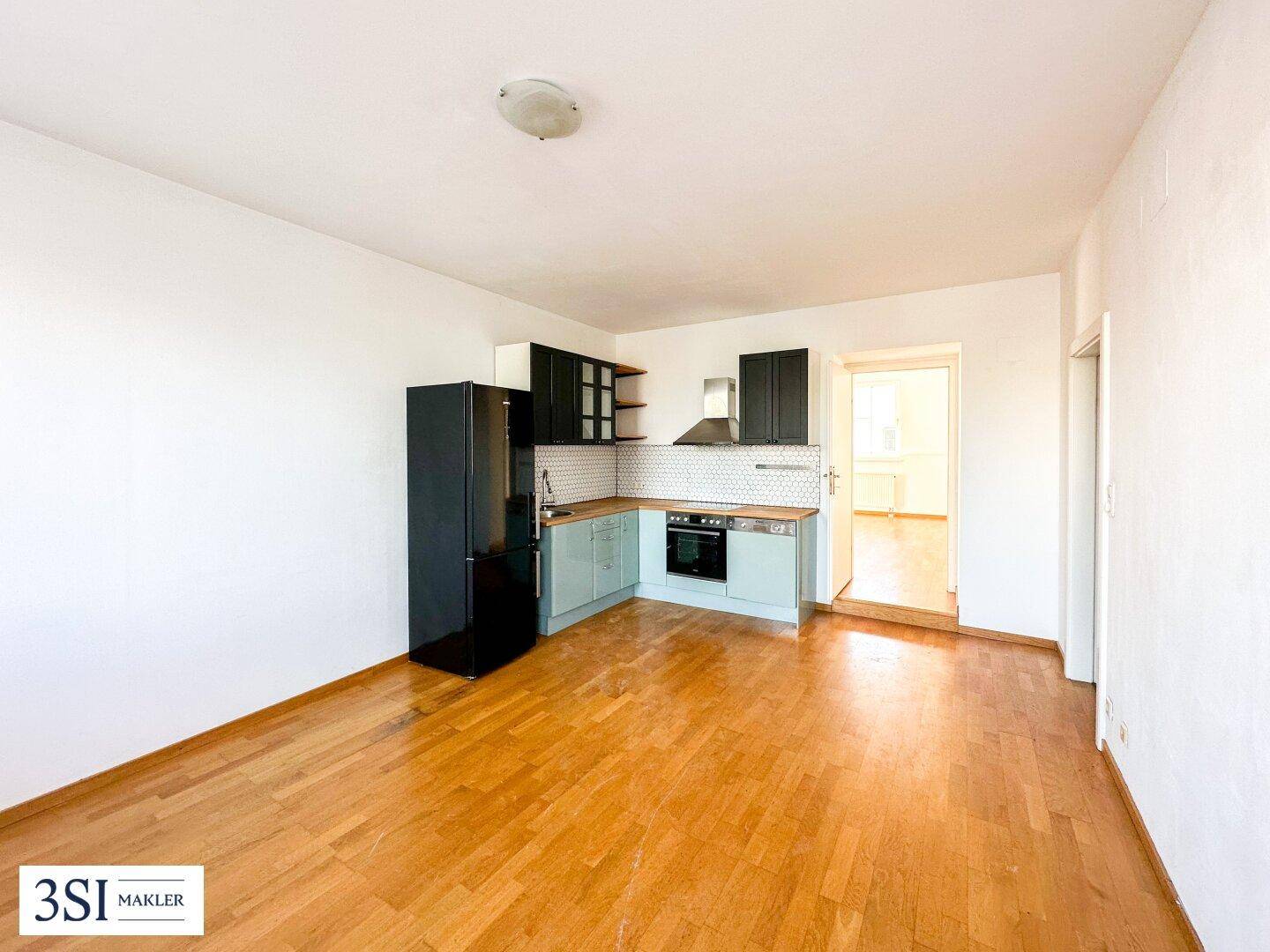 Offener Wohnbereich mit integrierter Küchenzeile, Holzboden und modernen Geräten.