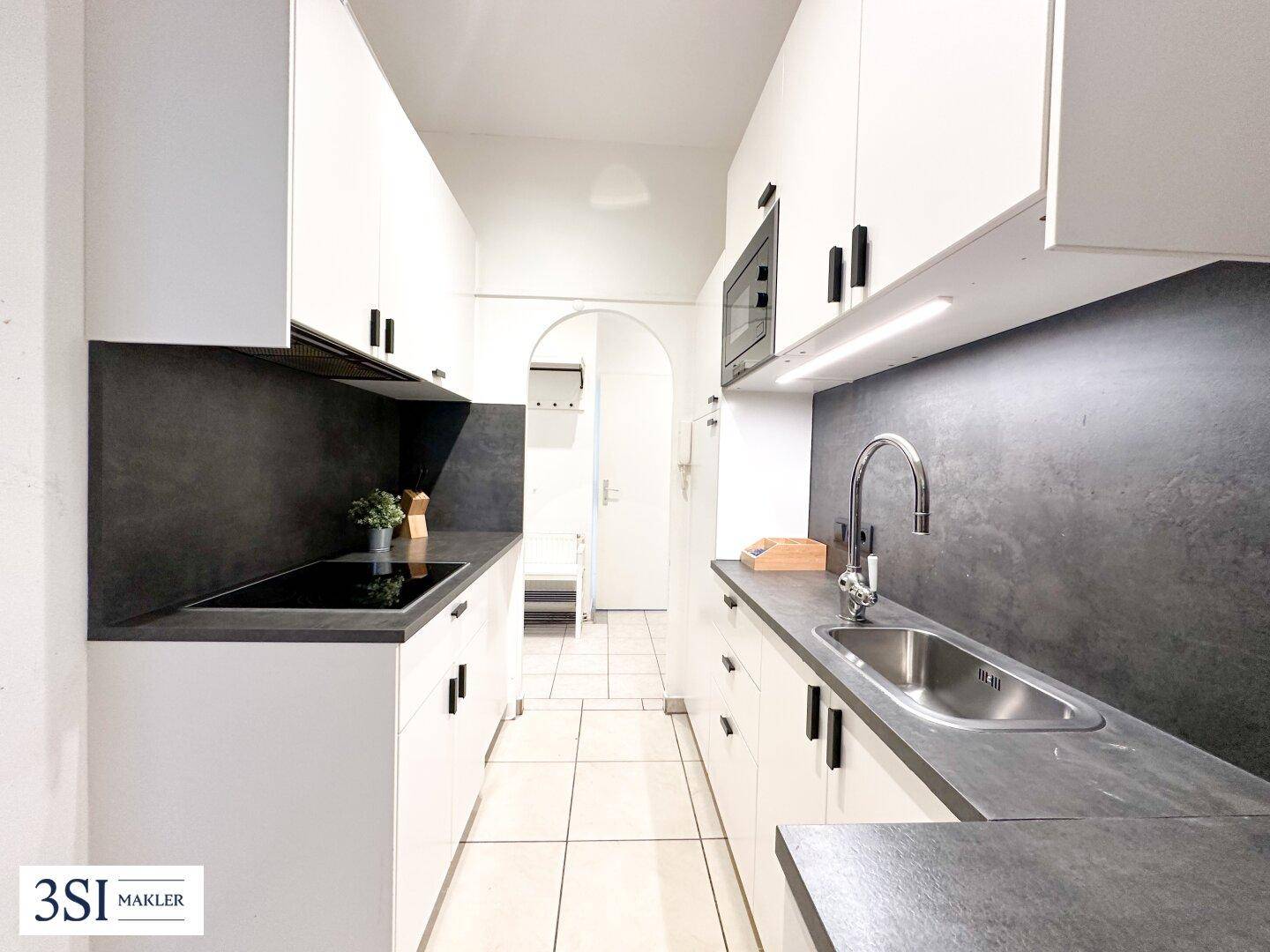 Moderne Küchenzeile mit weißen Schränken, dunkler Arbeitsplatte und Fliesenboden in schmalem Design.