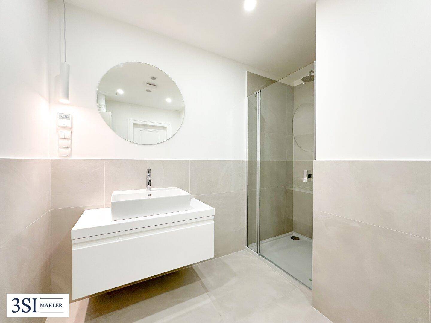 Helles, modernes Badezimmer mit minimalistischem Design, runden Spiegel und begehbarer Dusche.