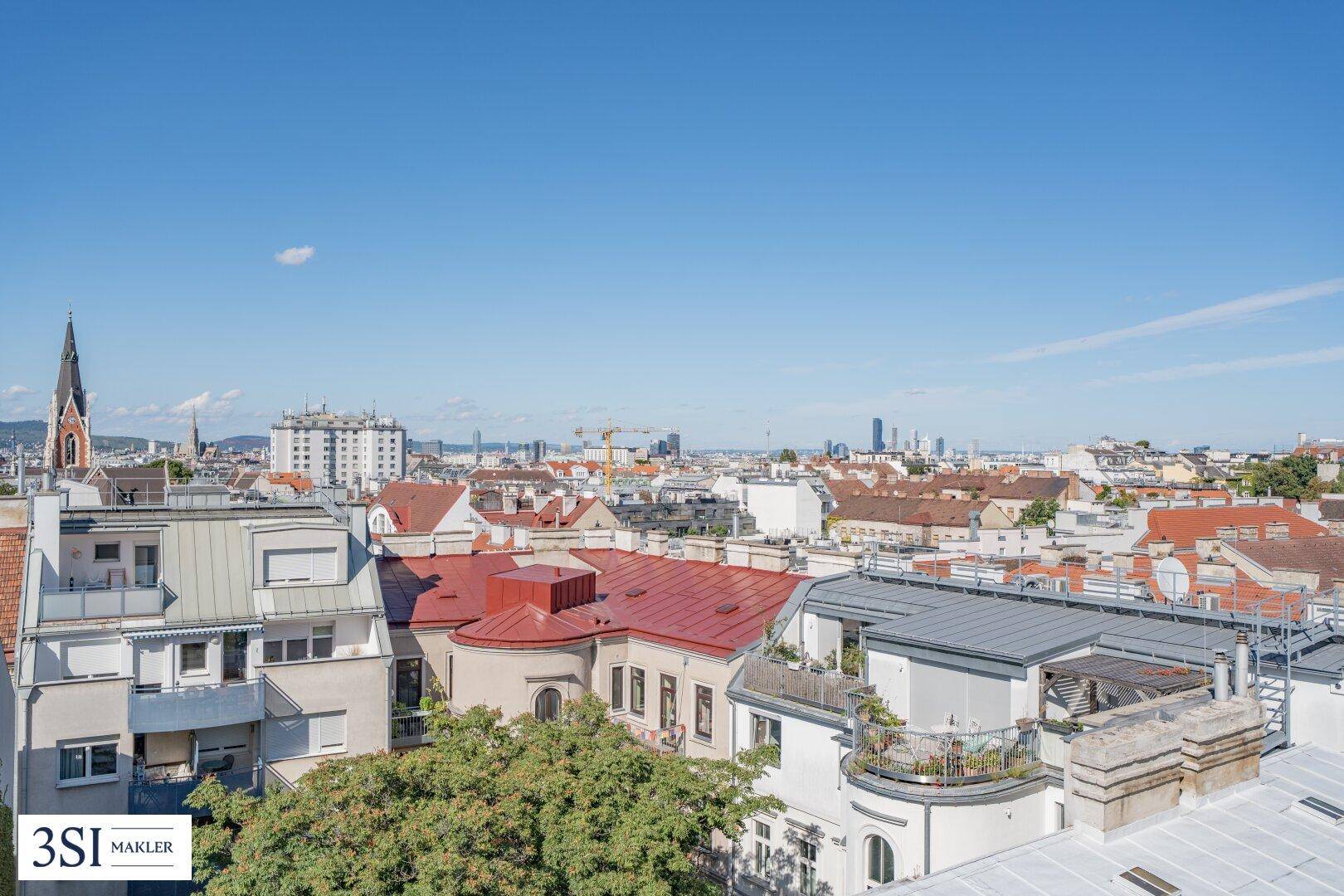 Weitläufiger Blick über die Dächer der Stadt mit historischer Architektur und moderner Skyline am Horizont.