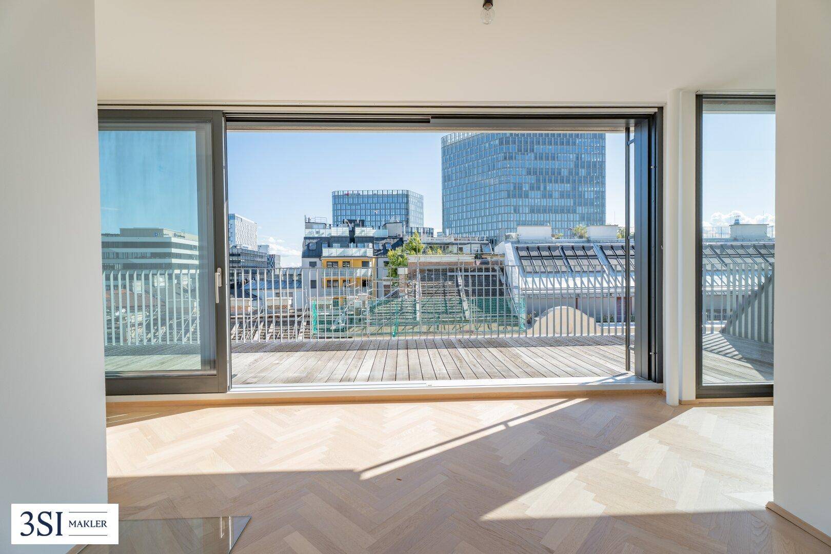 Blick aus dem Innenraum auf eine Holzterrasse mit urbaner Skyline und modernen Gebäuden im Hintergrund.