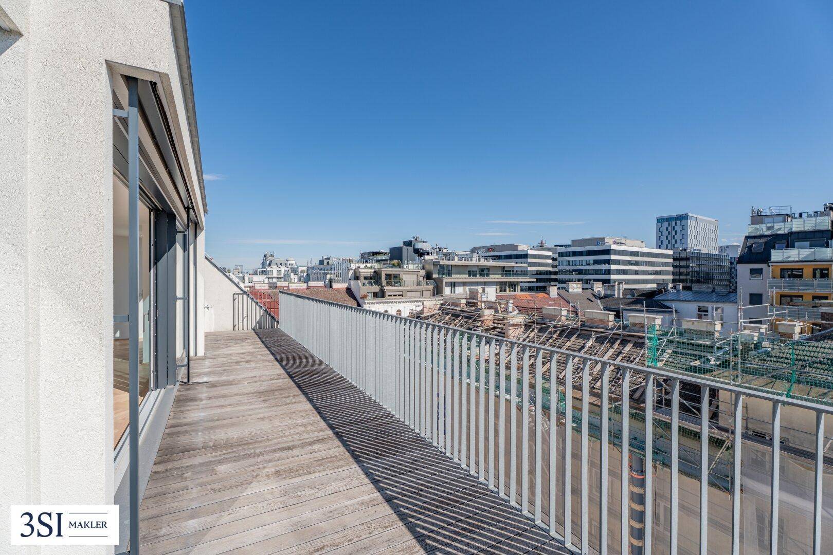 Lange Holzterrasse mit Metallgeländer und weitem Blick über die Dächer der Stadt.
