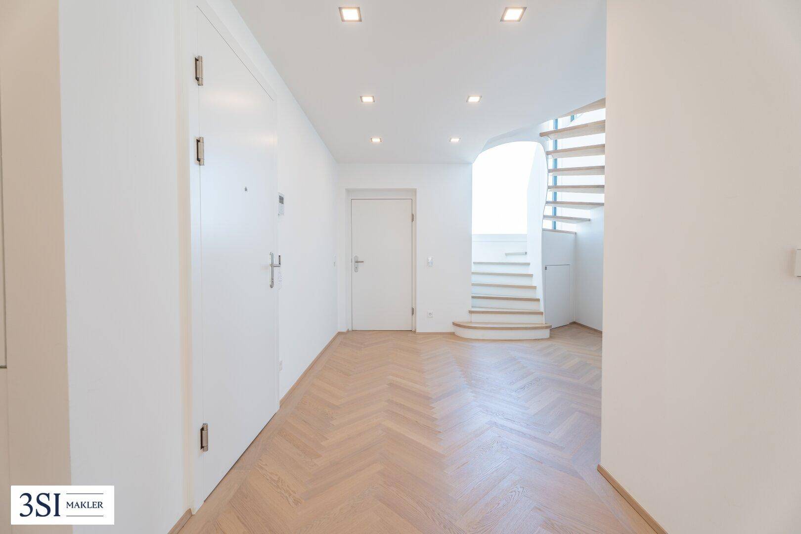 Heller Eingangsbereich mit Fischgrätparkett, Einbaustrahlern und einer eleganten Wendeltreppe.